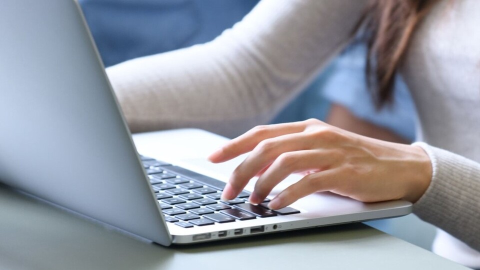 Eine Studentin schreibt an einem Laptop, im Bild sind die Arme, die linke Hand am Laptop, der Oberkörper und lange braune Haare. Das Laptop steht auf einem Tisch im ExpLAB im Bibliotheksbereich Schloss Schneckenhof.