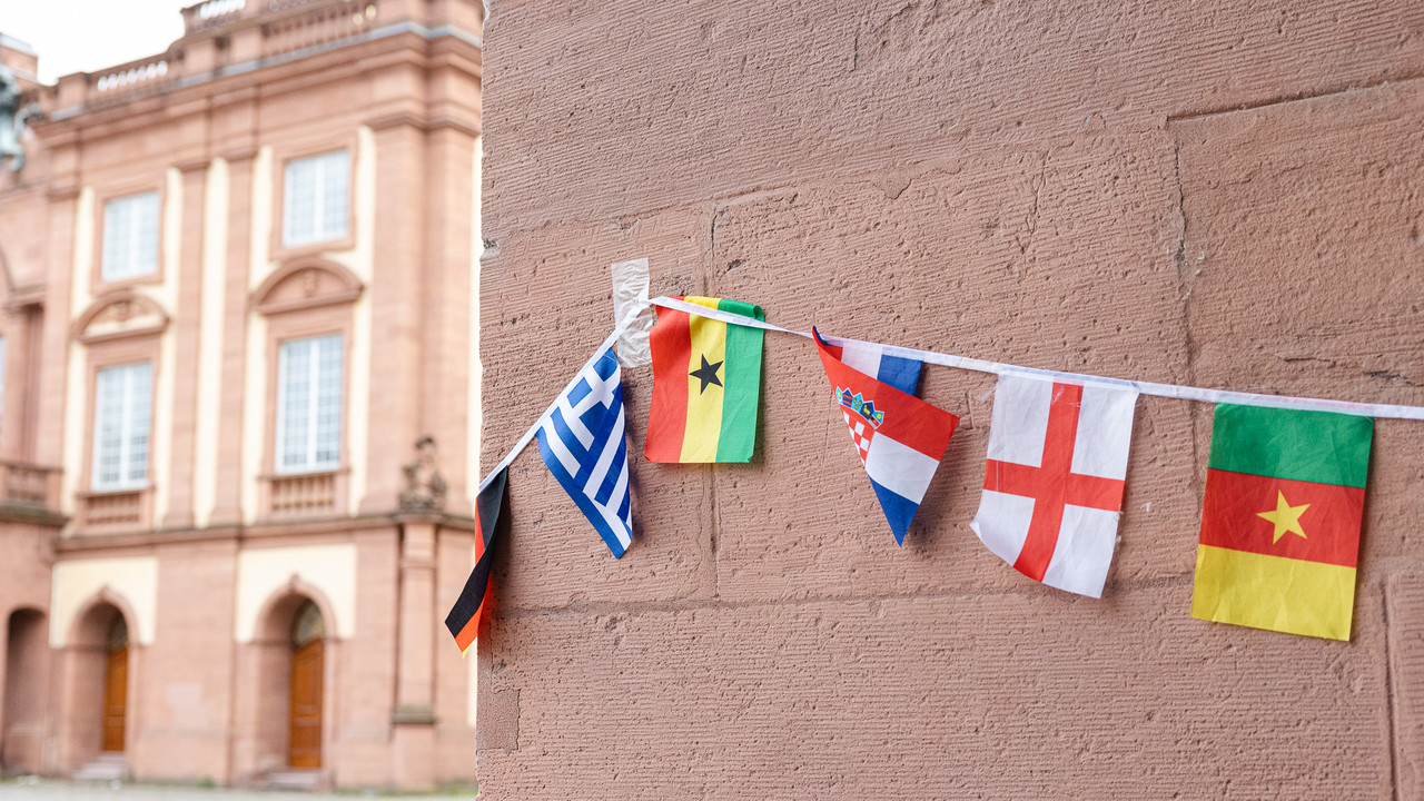 Um eine Säule des Schlosses Mannheim hängen viele bunte Landesflaggen, z.B. von Griechenland, Ghana und Kamerun.