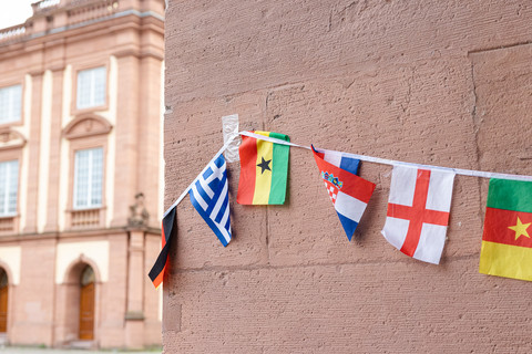 Um eine Säule des Schlosses Mannheim hängen viele bunte Landesflaggen, z.B. von Griechenland, Ghana und Kamerun.