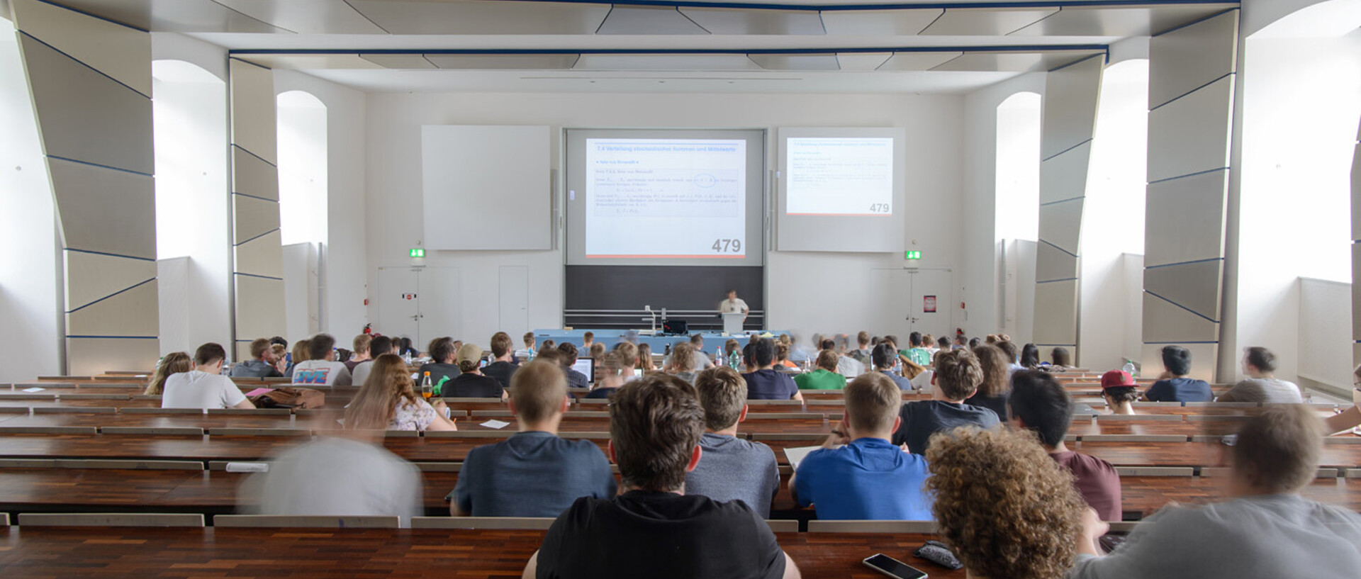 Studierende in einem Hörsaal mit Blick auf den Dozierenden an der Tafel