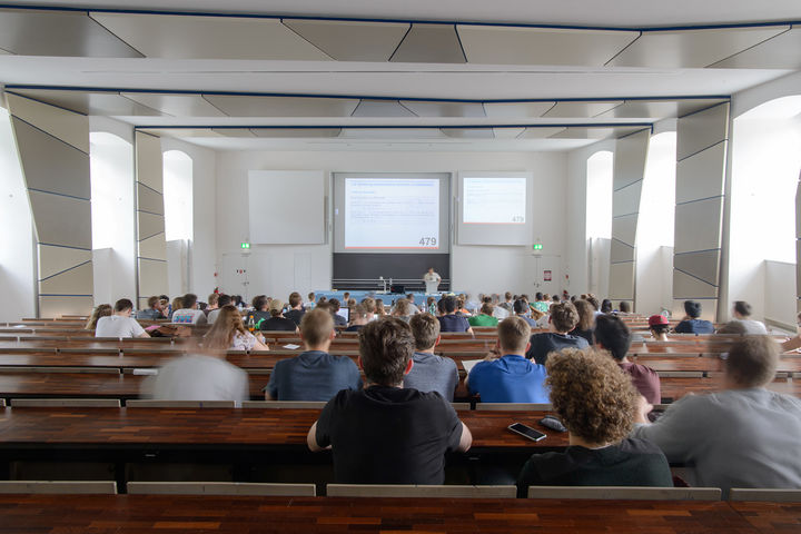 Studierende in einem Hörsaal mit Blick auf den Dozierenden an der Tafel