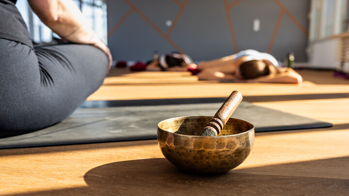Eine Klangschale im Bildfokus. Daneben der Oberschenkel einer Teilnehmerin des Yoga-Kurses, die auf einer Matte sitzt.