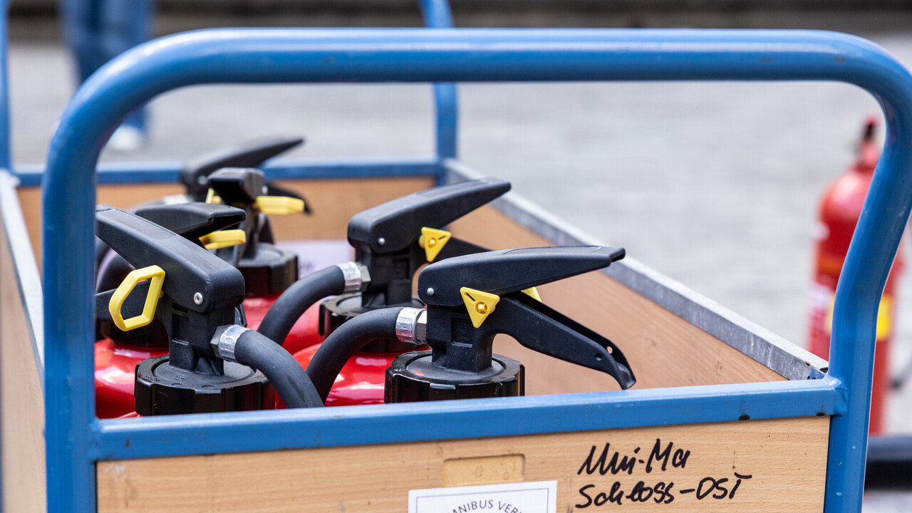 Ein hölzerner Rollwagen mit blauen Griffen, der das Logo der Universität Mannheim trägt. In dem Rollwagen stehen mehrere Feuerlöscher.
