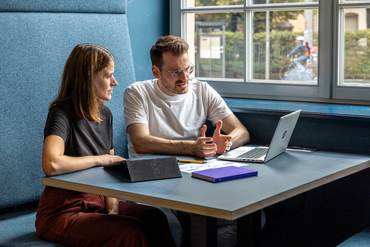 Ein Mann und eine Frau sitzen gemeinsam an einem Tisch und schauen konzentriert auf einen Laptop.