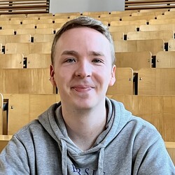 Kevin Seibel sitzt in einem leeren Hörsaal der Uni. Er hat kurze blonde Haare und trägt einen Hoodie der Uni Mannheim.