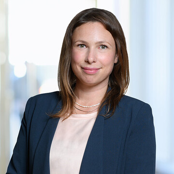Porträt von Jule Leger. Sie trägt ein dunkelblaues Sakko und lächelt in die Kamera.