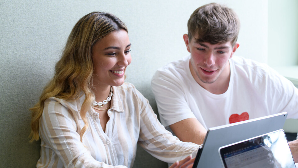 Eine Studentin und ein Student sitzen vor einem Tablet.