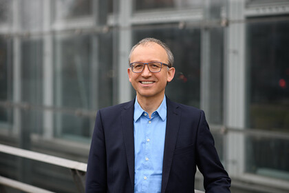 Portrait of Professor Thomas Gschwend, Ph.D. He is wearing a blue shirt with a dark jacket over it and is leaning against a railing.