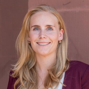 Kristin Schorb has long blonde hair and wears a light-colored blouse and a red jacket