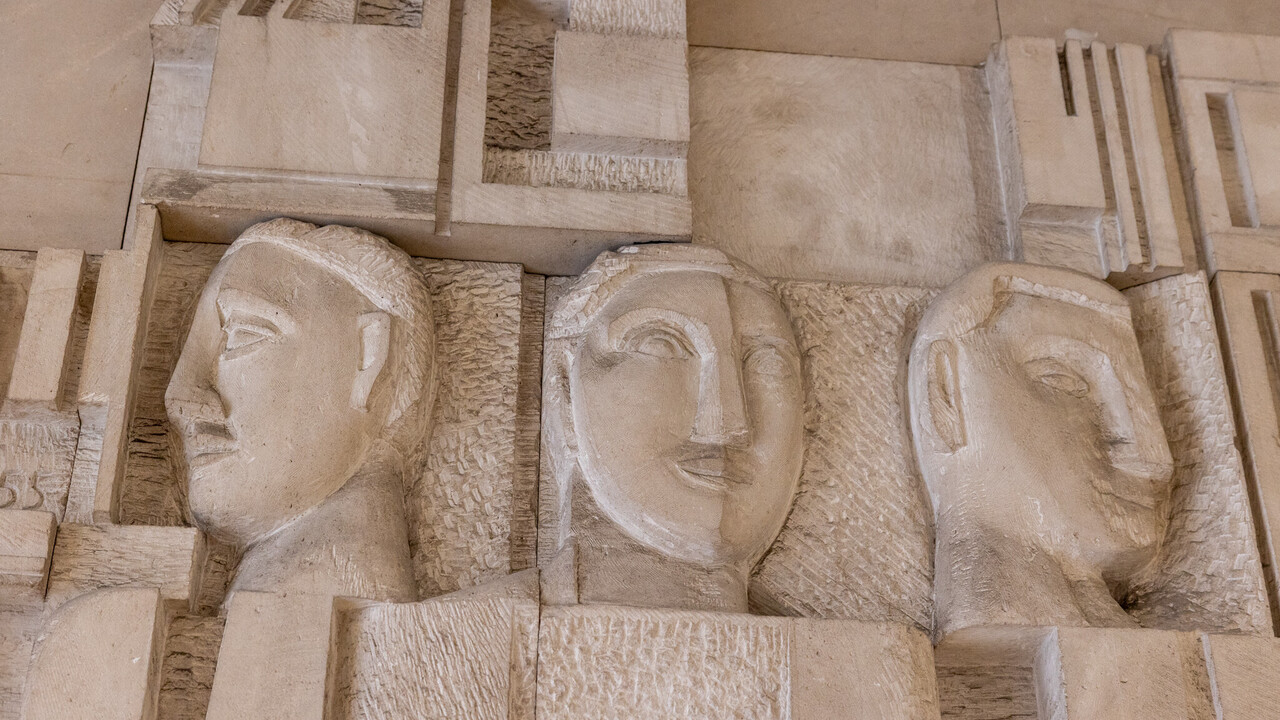 In einer Steinmauer sind drei Gesichter eingemeißelt.