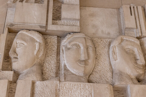 In einer Steinmauer sind drei Gesichter eingemeißelt.