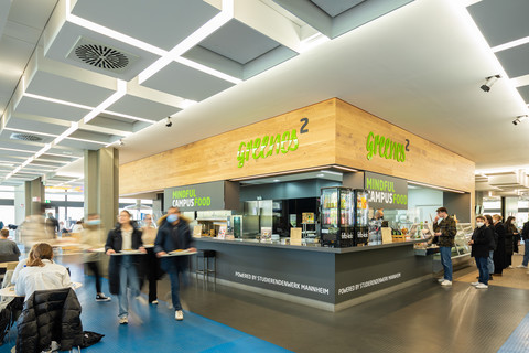 Eine moderne Theke aus Holz in der Mensa. Auf der Theke steht mit greller, grüner Schrift "greenes²" und "mindful campus food".