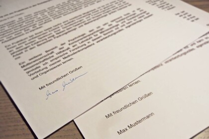 Zwei maschinell erstellte Schreiben liegen auf einem Tisch, eins wurde händisch unterschrieben.