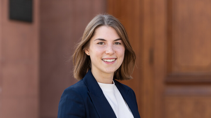 Anna-Lena Herforth. She has long brown hair and is wearing a white shirt and black blazer..
