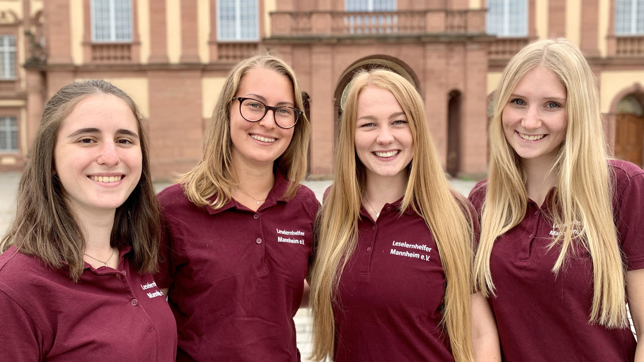 Vier Studentinnen lächeln. Sie tragen alle lange, offene Haare und rote T-Shirts mit der Aufschrift "Leselernhelfer Mannheim e.V.".