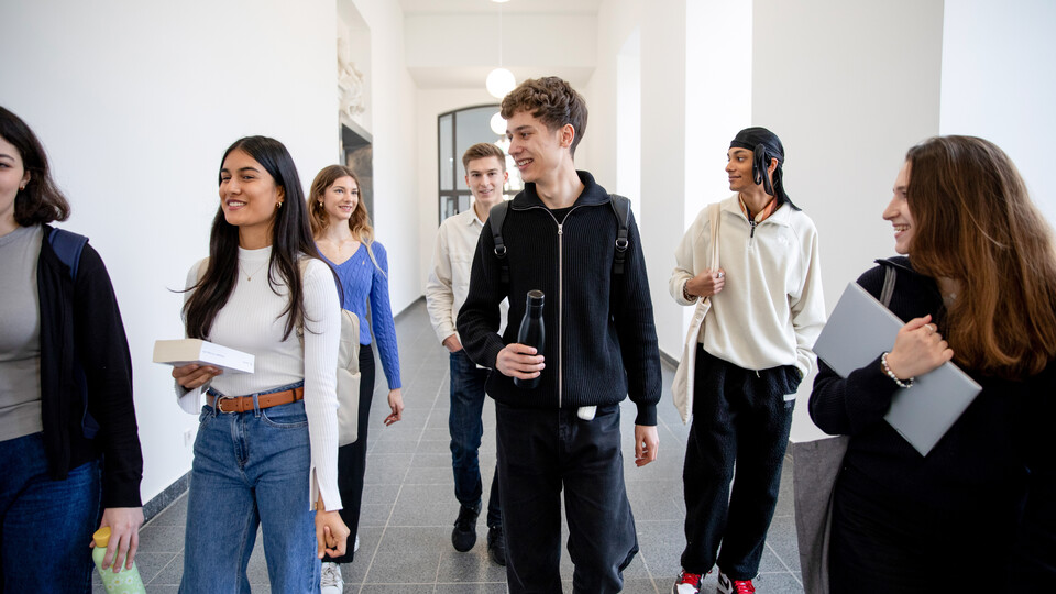 Gruppe Studierender laufen einen Flur im Schloss entlang und unterhalten sich