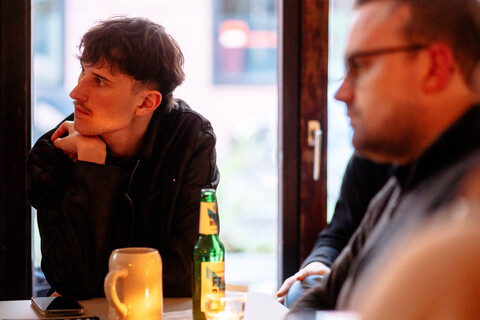 Zwei Personen sitzen an einem Tisch und schauen nach links. Auf dem Tisch stehen verschiedene Getränke.