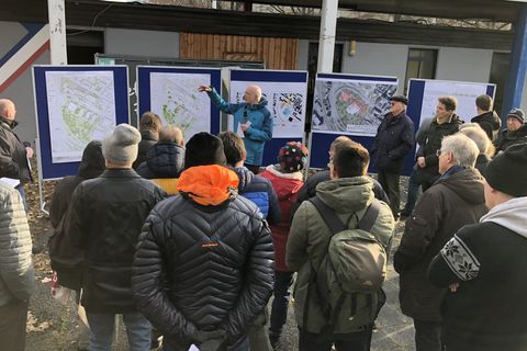 Rektor Prof. Dr. Thomas Puhl präsentiert die Pläne zur Bebauung des Friedrichparks. Er zeigt auf Plakate des Rahmenplans und Skizzen. Um ihn herum sind Zuschauende.  