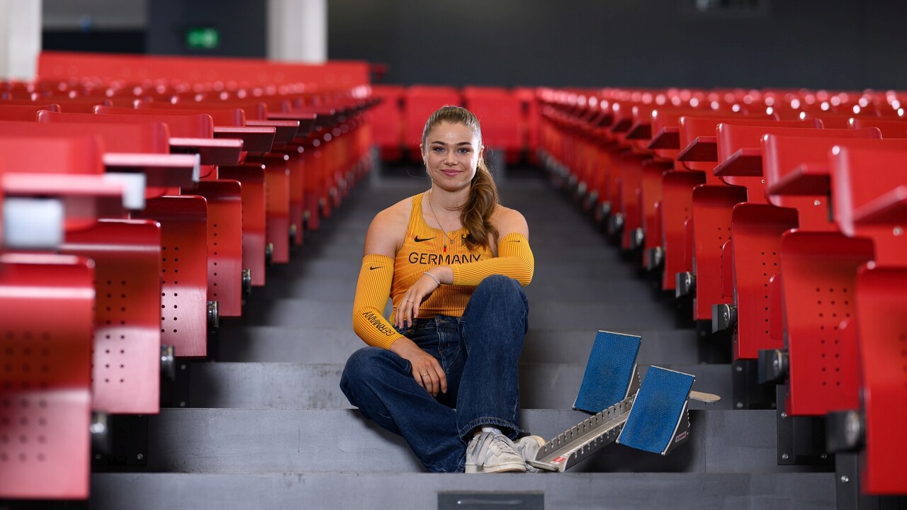 Eine Leichtathletikerin sitzt mit Startblöcken auf den Treppen eines Vorlesungssaals.
