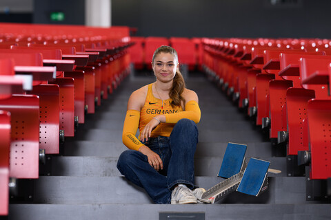 Eine Leichtathletikerin sitzt mit Startblöcken auf den Treppen eines Vorlesungssaals.