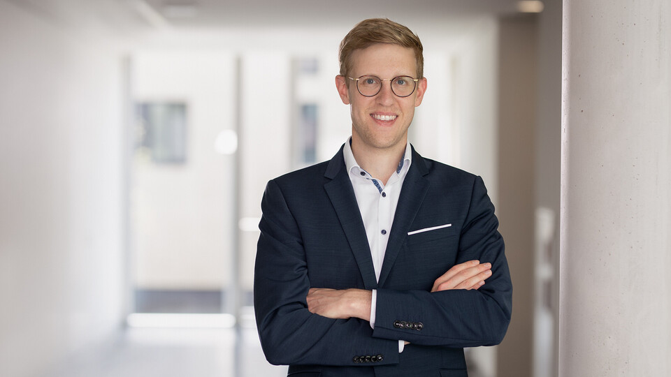 Jens Förderer. He is wearing a black suit inside a white walled building.