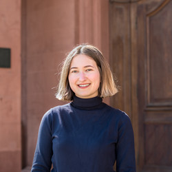 Laura Prosen wears a blue turtleneck sweater and stands in the castle courtyard.