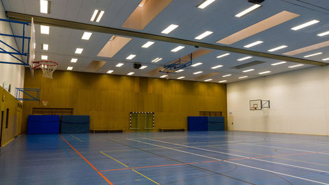 Die Unihalle mit Blick auf eine ockerfarbene Wand, an der dicke, blaue Sportmatten lehnen, mittig steht ein Fußballtor.