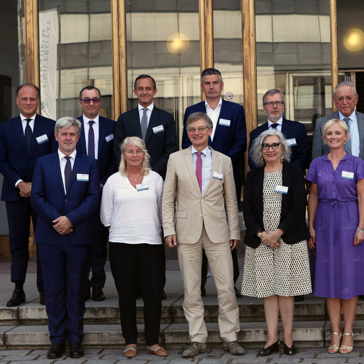 Eine Gruppe von Menschen des ALEUESS-Bündnis stehen vor dem Eingang der Uni. Sie tragen schicke Kleidung.