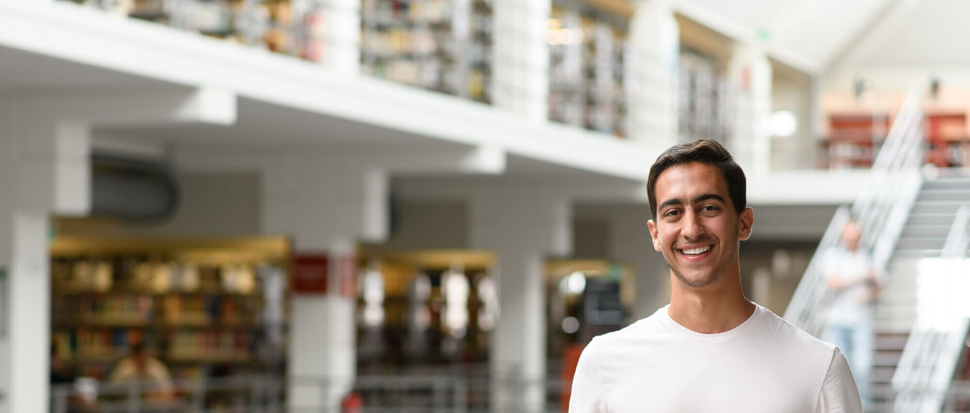 Ein Student steht im Bibliotheksbereich A3 und hält einen Stapel Bücher in den Händen.