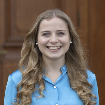 Tonia laughs brightly into the camera. She has long, dark blonde hair and is wearing a blue blouse.