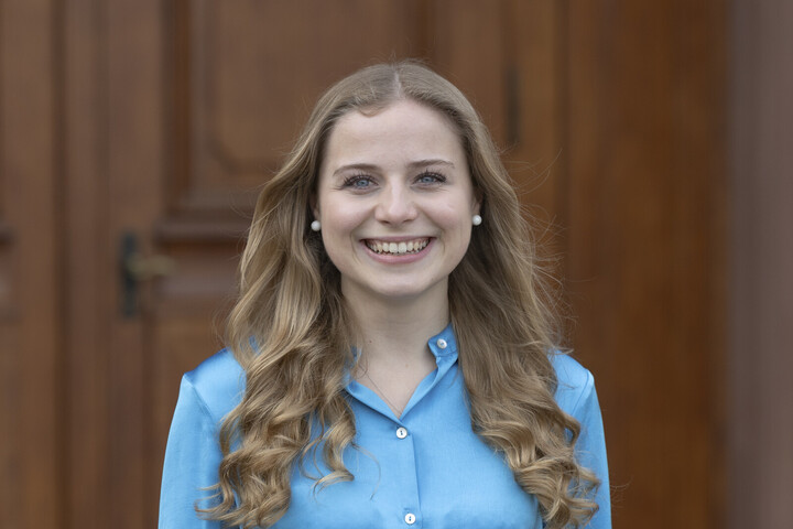 Tonia laughs brightly into the camera. She has long, dark blonde hair and is wearing a blue blouse.