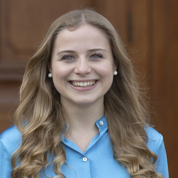 Tonia laughs brightly into the camera. She has long, dark blonde hair and is wearing a blue blouse.