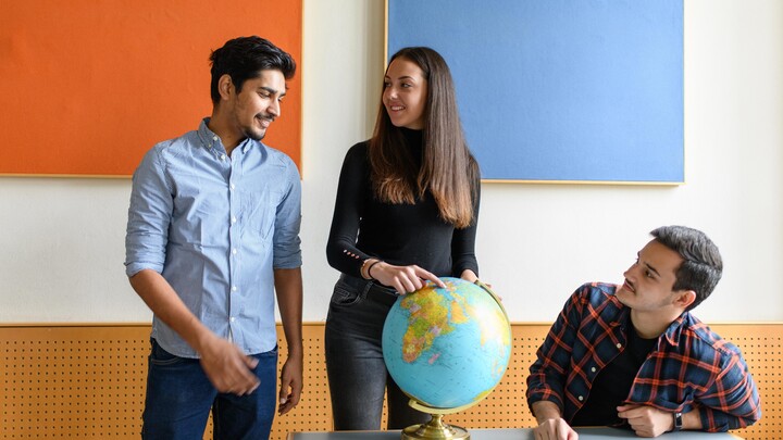 Eine Studierende zeigt zwei anderen Studierenden ein Land auf einem Globus.