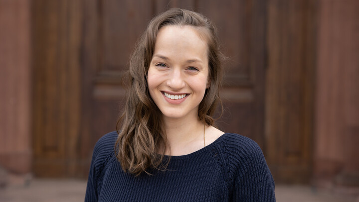 Monika Burckhardt. She is wearing a dark blue sweater and is standing in front of one of the castle doors.