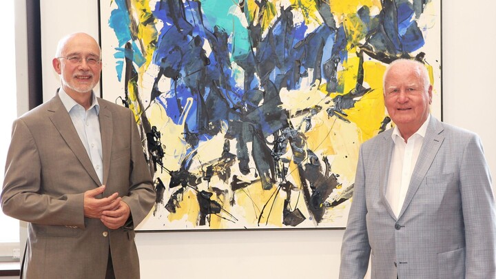Manfred Fuchs und Thomas Puhl stehen vor einem bunten, abstrakten Gemälde.