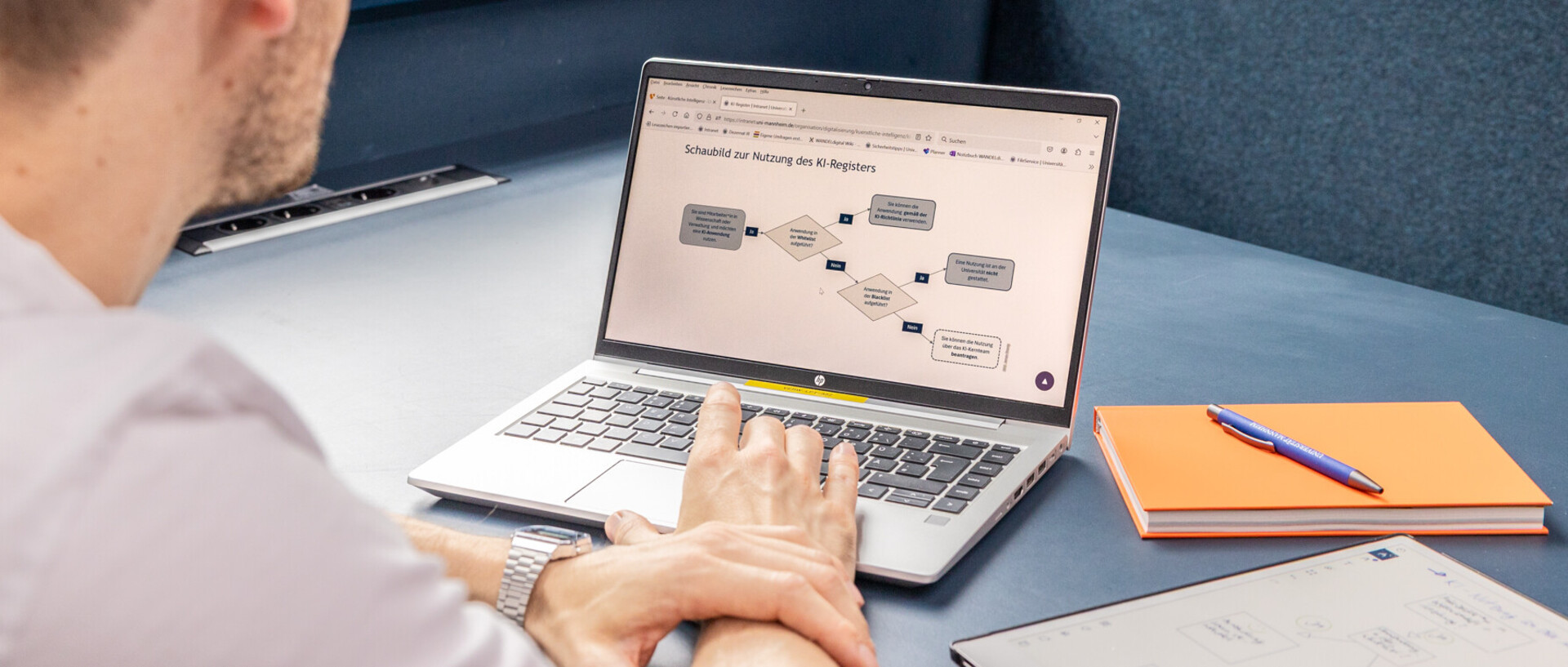 Ein Mitarbeiter bedient einen Laptop und hat ein Schaubild zur Nutzung des KI-Registers geöffnet.
