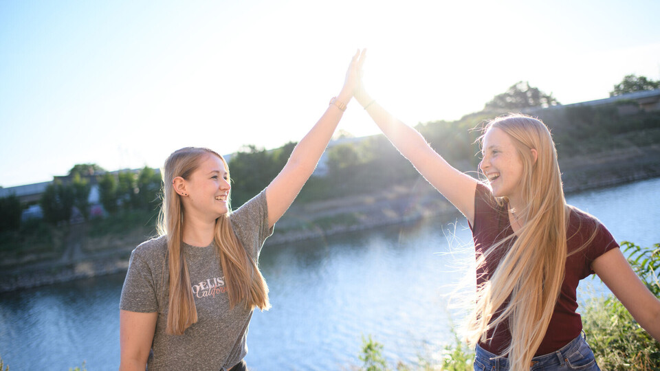 Zwei Studentinnen stehen am Neckarkanal und klatschen sich mit High-Five ab. Sie lachen und sind fröhlich.