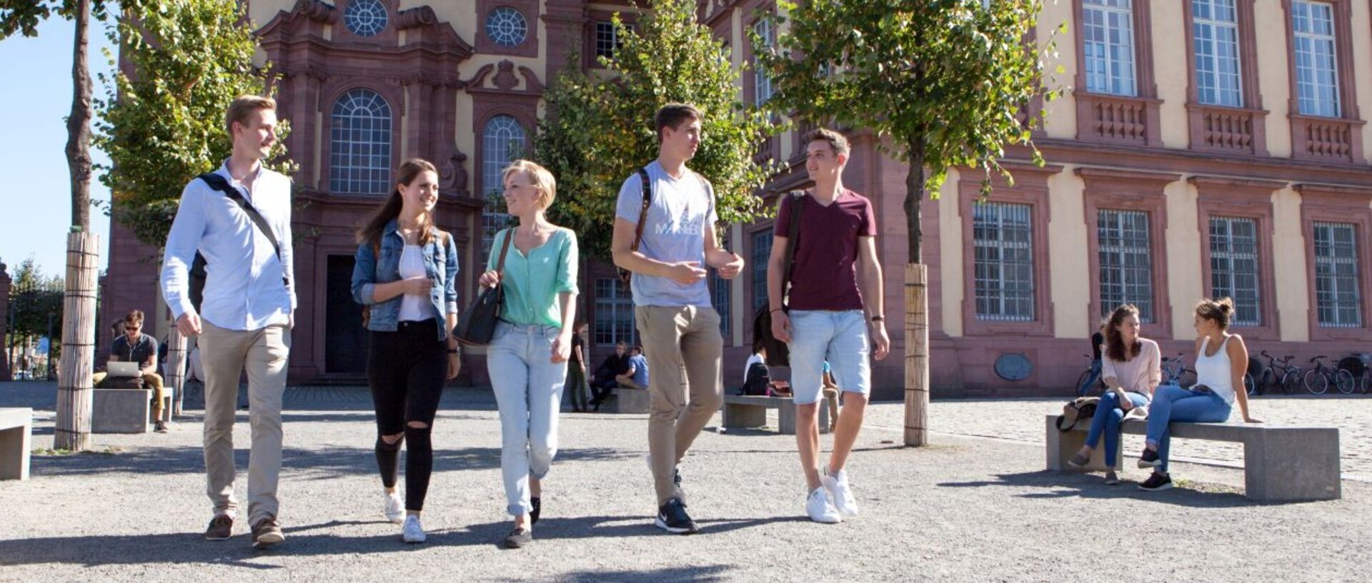 Studierende schlendern gut gelaunt über den sonnigen Ehrenhof der Uni Mannheim