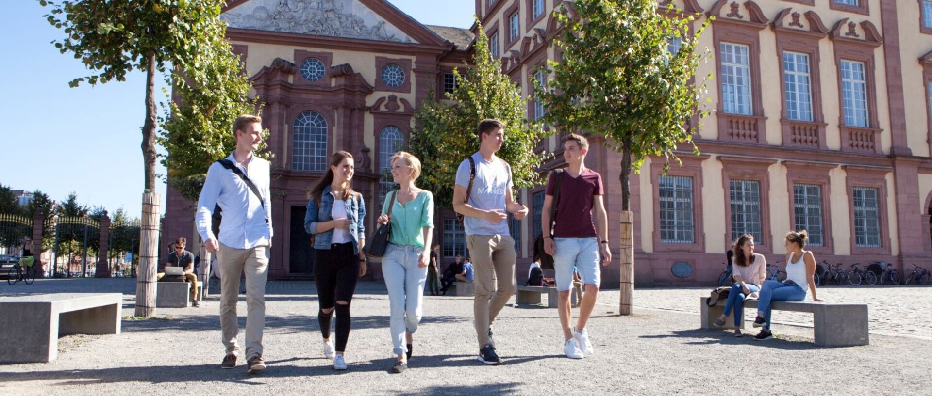 Studierende schlendern gut gelaunt über den sonnigen Ehrenhof der Uni Mannheim