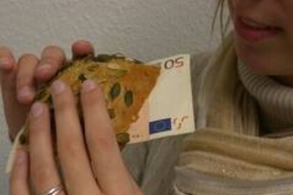 Die Hände einer Frau führen ein Brötchen, aus dem ein 50-Euro-Schein herausschaut, zu ihrem Mund.