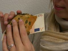 Die Hände einer Frau führen ein Brötchen, aus dem ein 50-Euro-Schein herausschaut, zu ihrem Mund.
