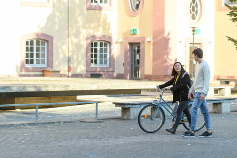 Zwei Studierende laufen durch den Schneckenhof, die Studentin schiebt ihr Rad.