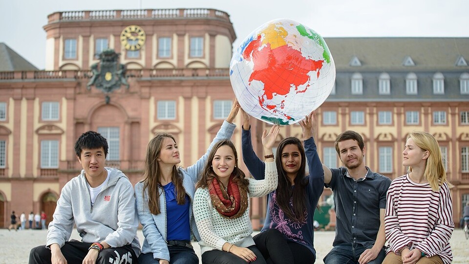 Abgebildet ist eine Gruppe von Studierenden, die gemeinsam eine Weltkugel hochhalten.