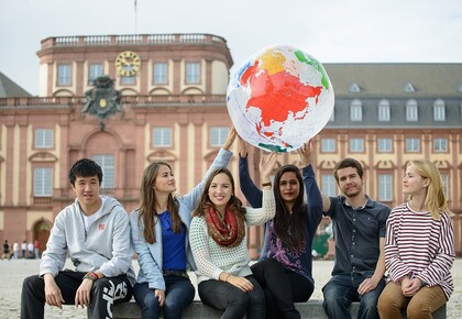 Abgebildet ist eine Gruppe von Studierenden, die gemeinsam eine Weltkugel hochhalten.
