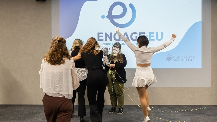 Mehrere Personen freuen sich, eine springt in die Luft. Im Intergrund ist das ENGAGE.EU-Logo zu sehen.