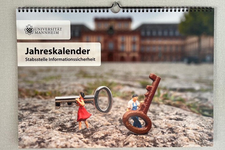 Titelbild des Jahreskalenders der Stabsstelle Informationssicherheit. Zu sehen sind zwei Miniatur-Figuren, die Schlüssel vor dem Schloss Mannheim tragen.