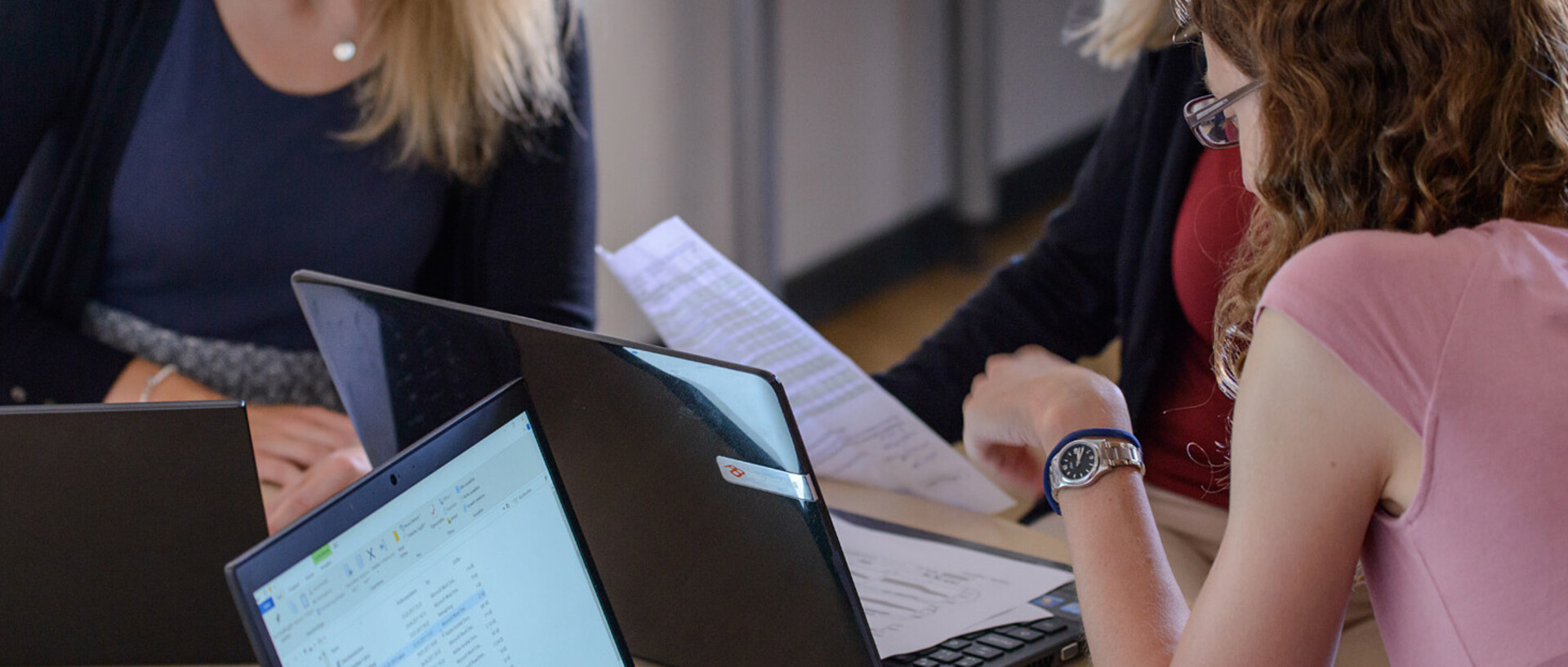 Drei Studentinnen sitzen mit ihren Laptops an einem Tisch und lernen gemeinsam.