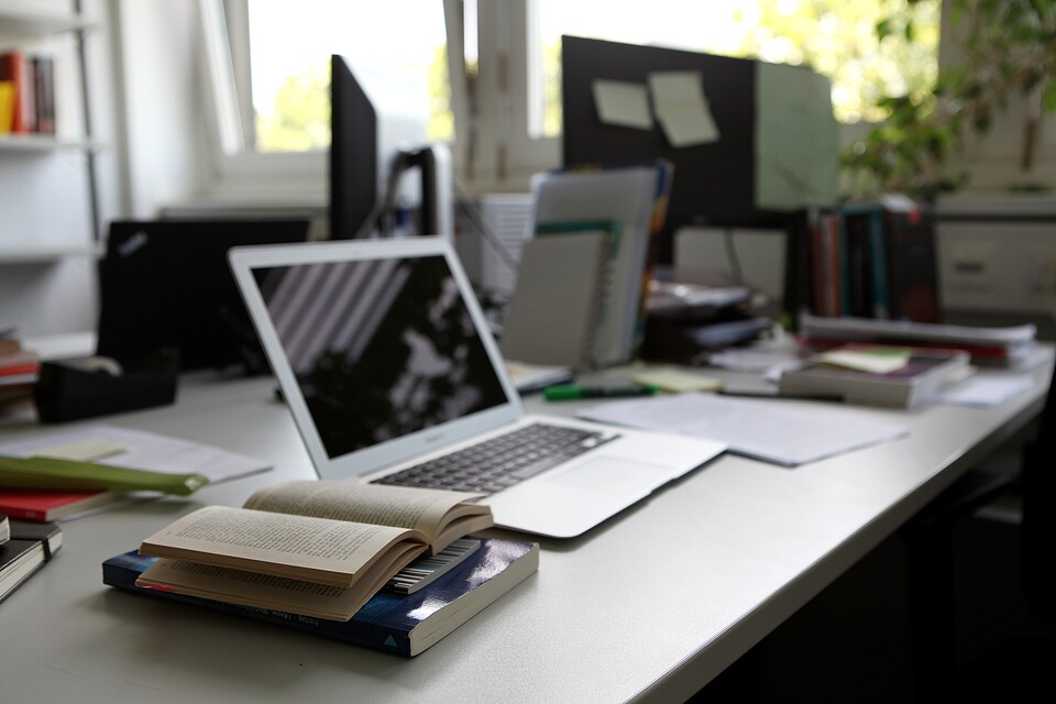Büro mit aufgeklapptem Laptop und aufgeschlagenem Buch auf Schreibtisch