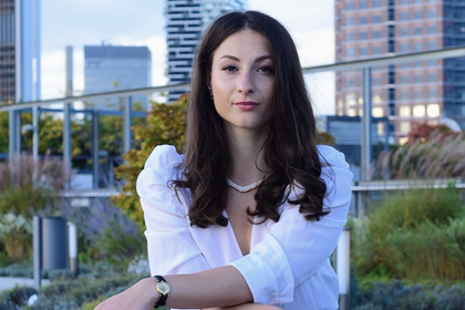 Giuliana Manganaro sitzt im Freien auf einer Bank. Sie hat lange dunkle Haare, trägt eine weiße Bluse und einen schwarzen Rock.