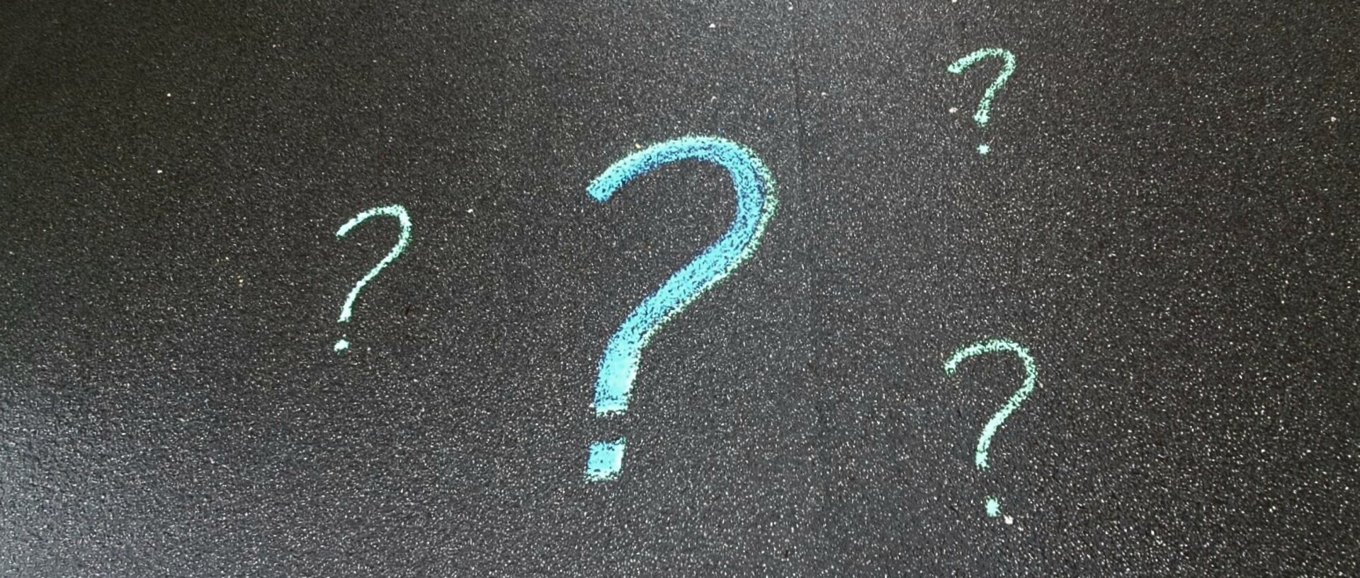 Mit blauer Kreide auf den Asphalt gezeichnete Fragezeichen
